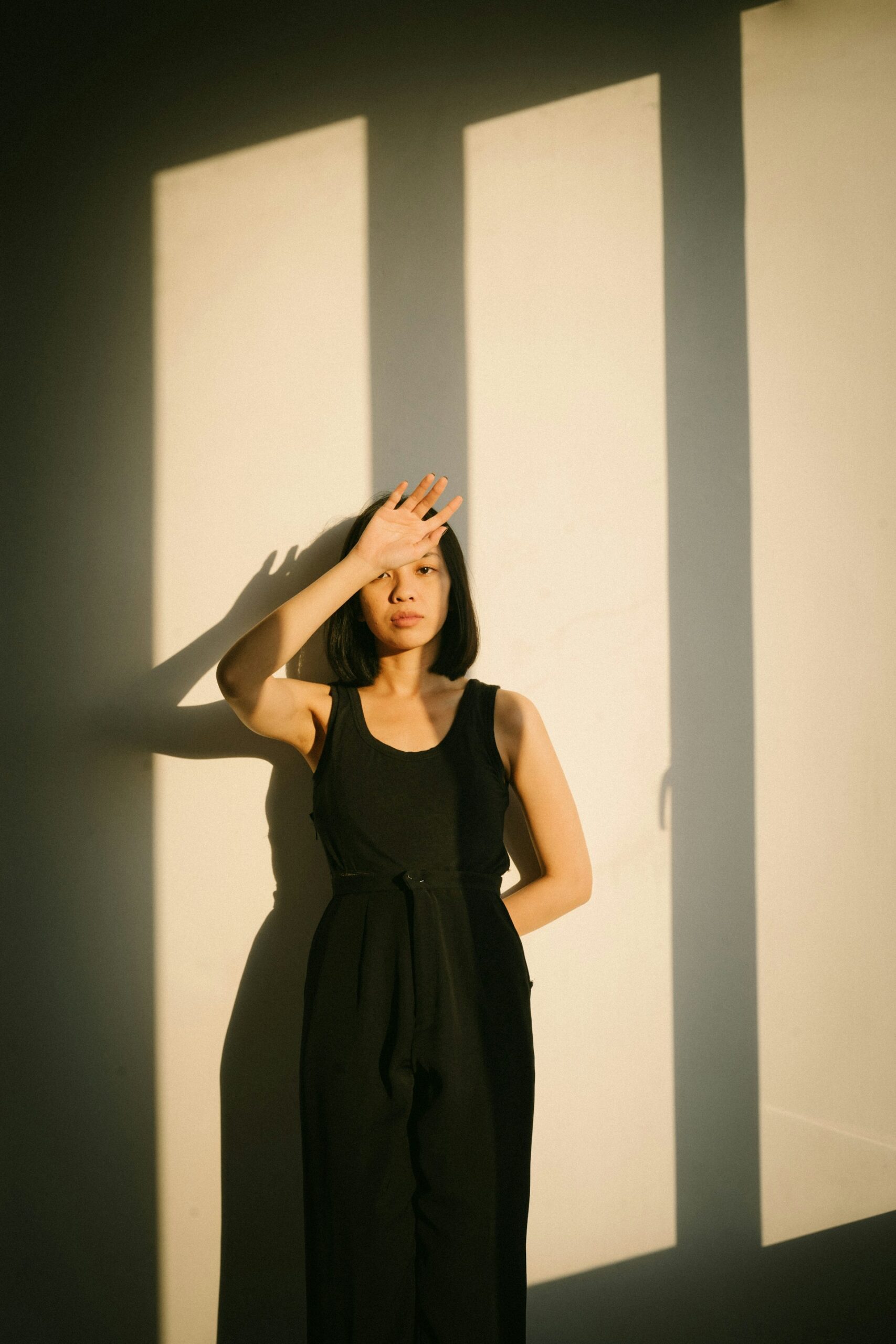 A woman stands in a sunlit room with her hand over her forehead