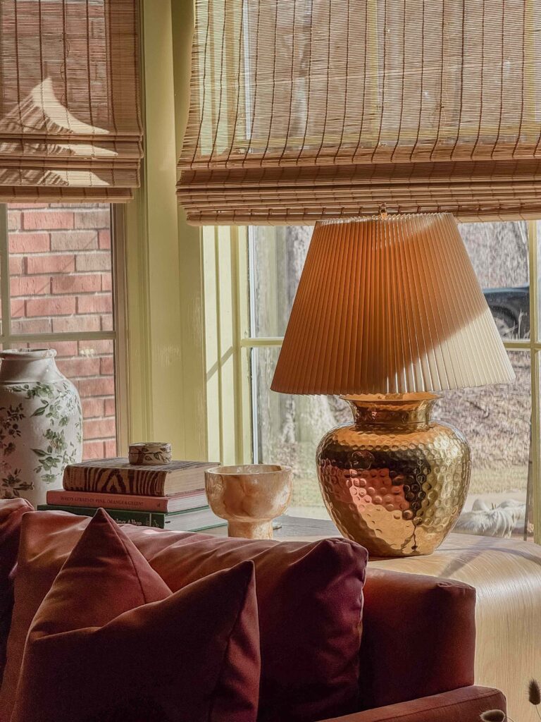 A golden lamp sits on a wooden console table in front of a picture window.