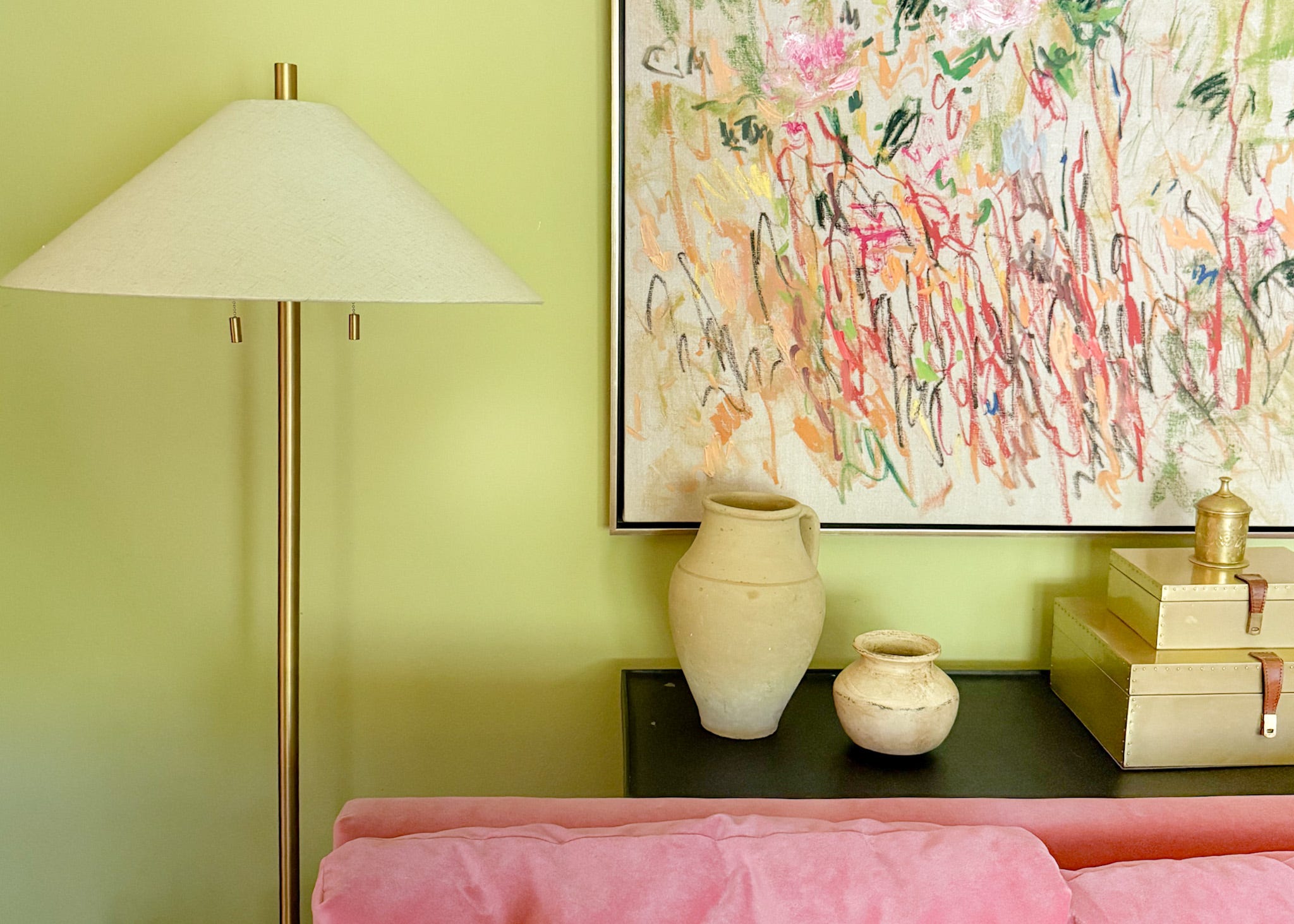 A pink sofa with a console table and floor lamp behind it, and abstract garden artwork from Anthropologie on the wall.